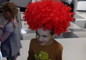 Chłopiec w czerwonej peruce na głowie.